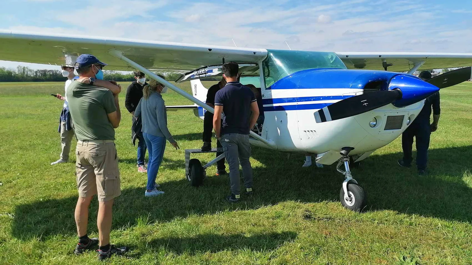 Student pilots and an instructor gathered around a light training aircraft on a grass airfield